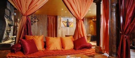 A room with a sofa set, a coffee table with a vase and rose petals, and curtains.