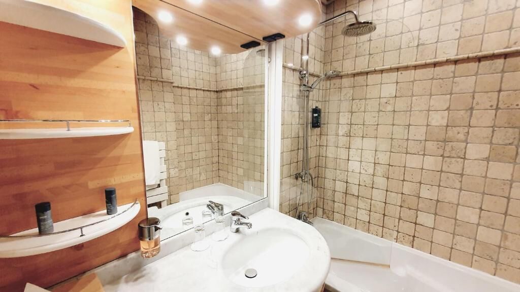 A bathroom with a wooden vanity, a sink, a mirror, and a shower area.