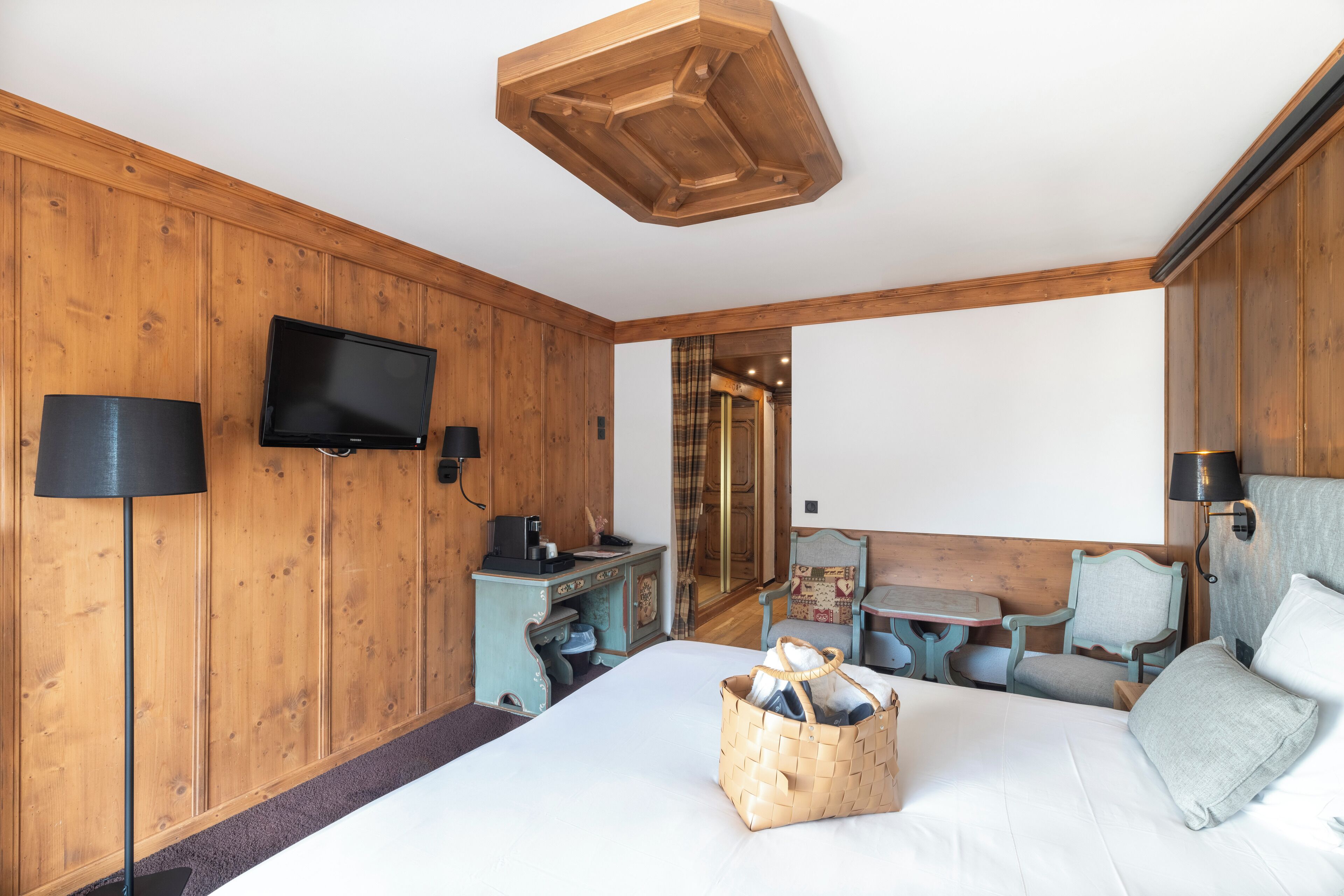 A wooden-paneled room with a bed, a desk, a television, and a table with chairs.