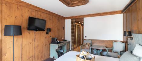 A wooden-paneled room with a bed, a desk, a television, and a table with chairs.