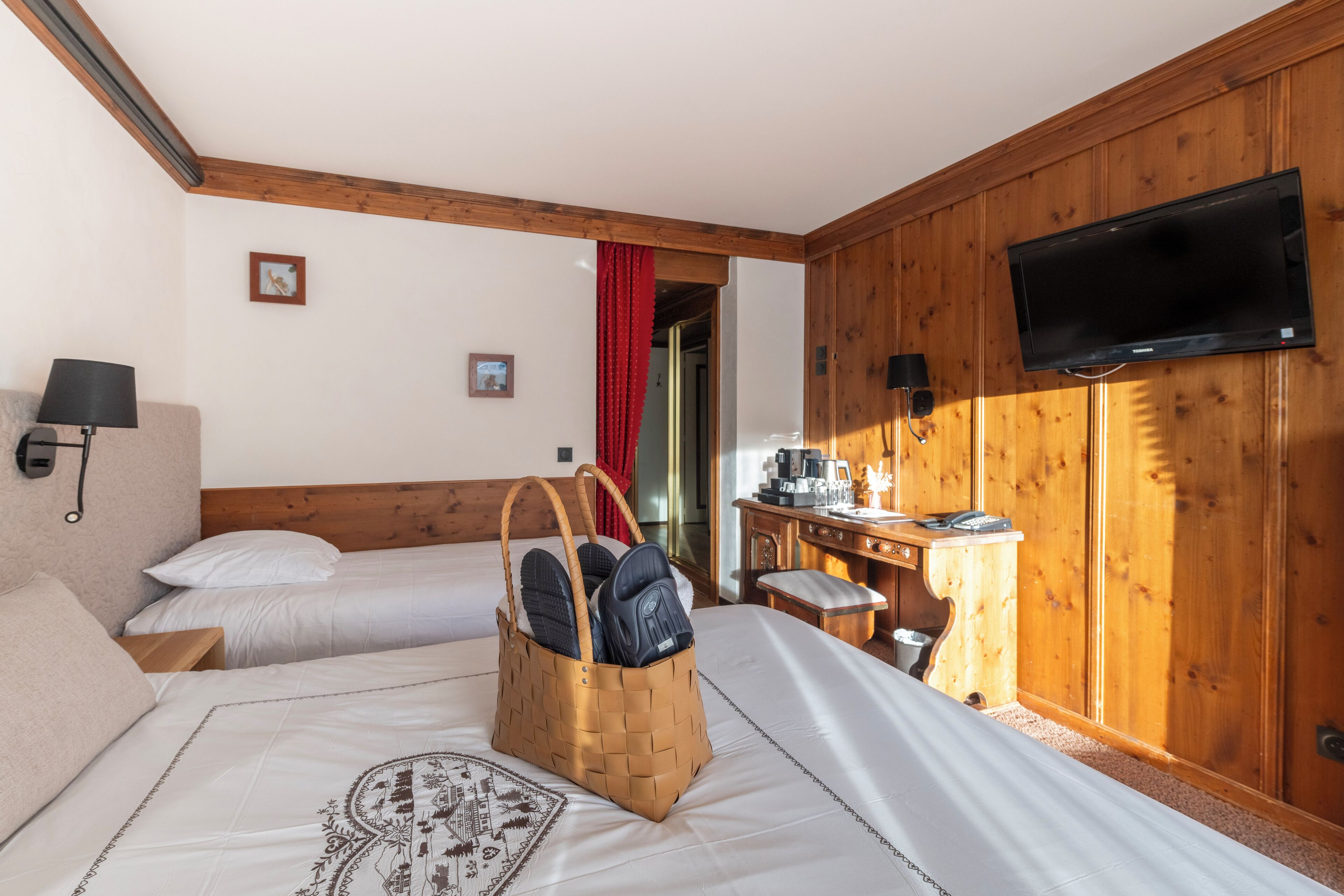 Ein Hotelzimmer mit zwei Betten, einem Holzschrank, einem Fernseher und einem Schreibtisch mit Stuhl.