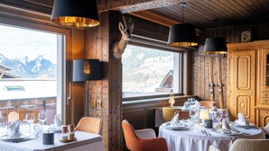 A dining area with tables set for a meal, wooden walls, and a view of mountains through a window. - Hôtel Macchi Restaurant & Spa (Chatel)