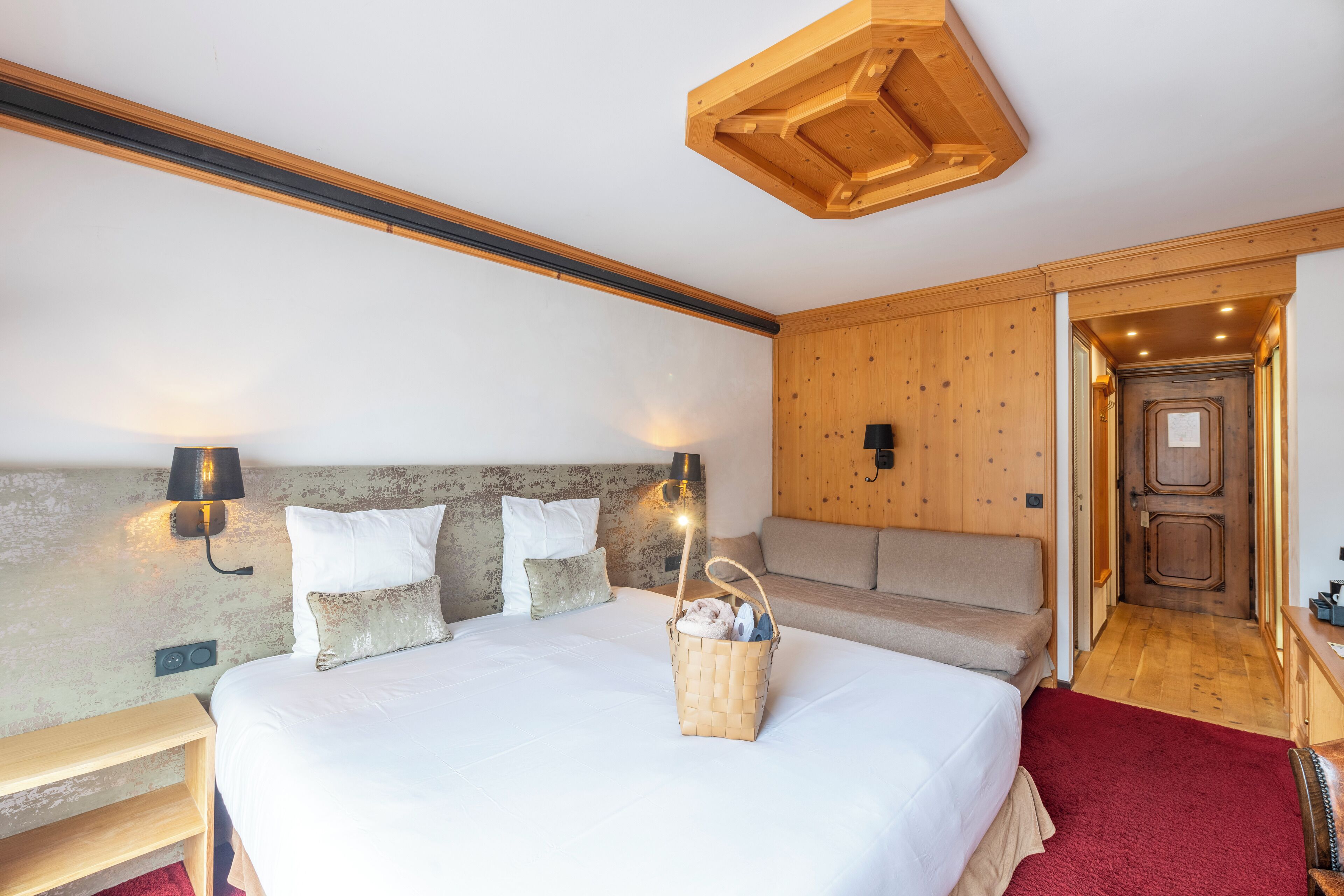 Een slaapkamer met een groot bed, een houten hoofdbord, twee wandlampen, een rood tapijt en een houten deur.