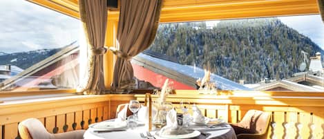 Un coin repas avec une table dressée pour quatre personnes, une rambarde en bois et une vue sur un paysage montagneux.