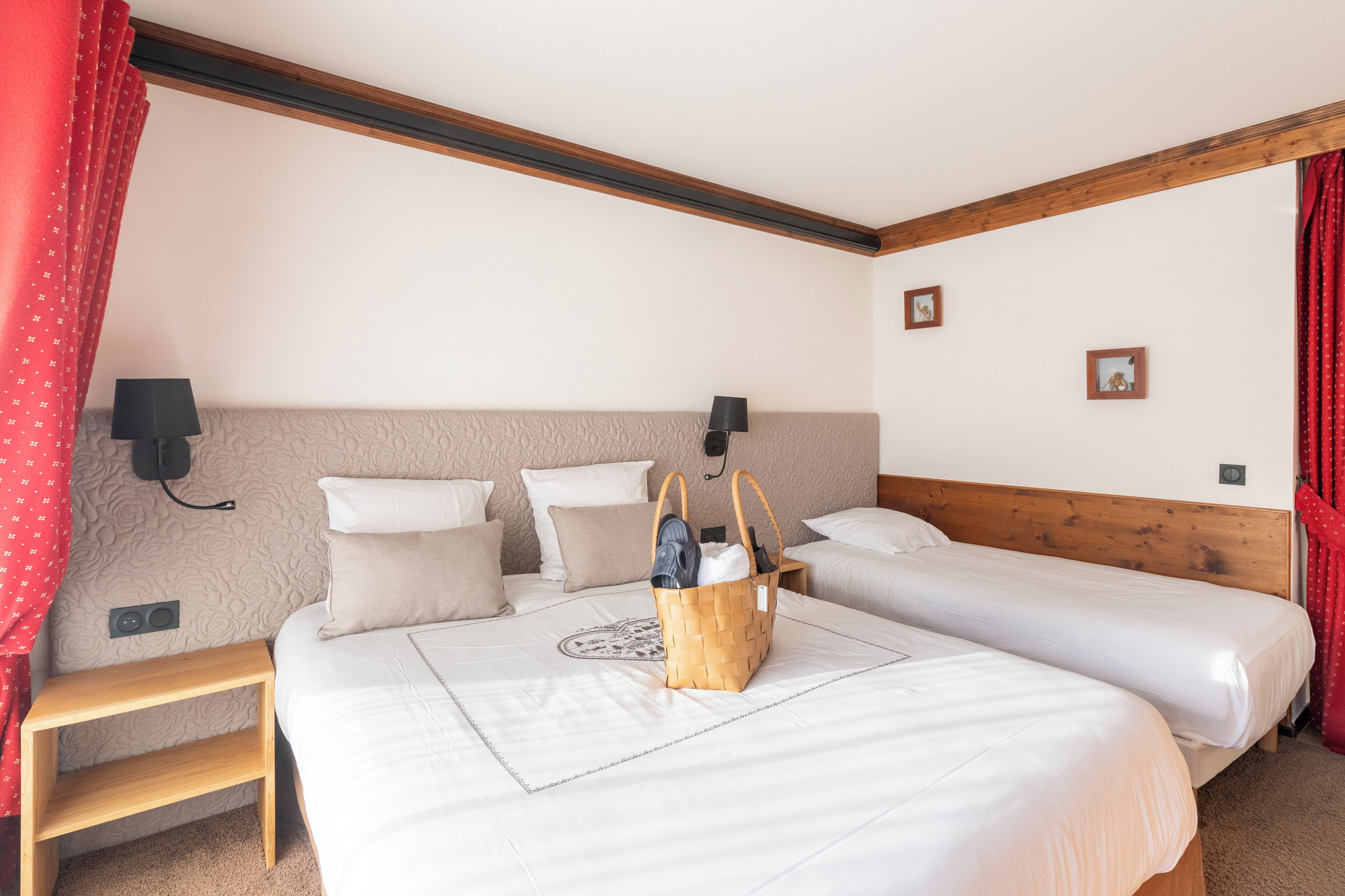 A bedroom with two single beds, a wooden headboard, a bedside table, and a basket on the bed.