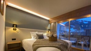 A modern hotel room with a large bed, a nightstand, a lamp, and a view of a mountain landscape through a large window. - Hôtel Macchi Restaurant & Spa (Chatel)