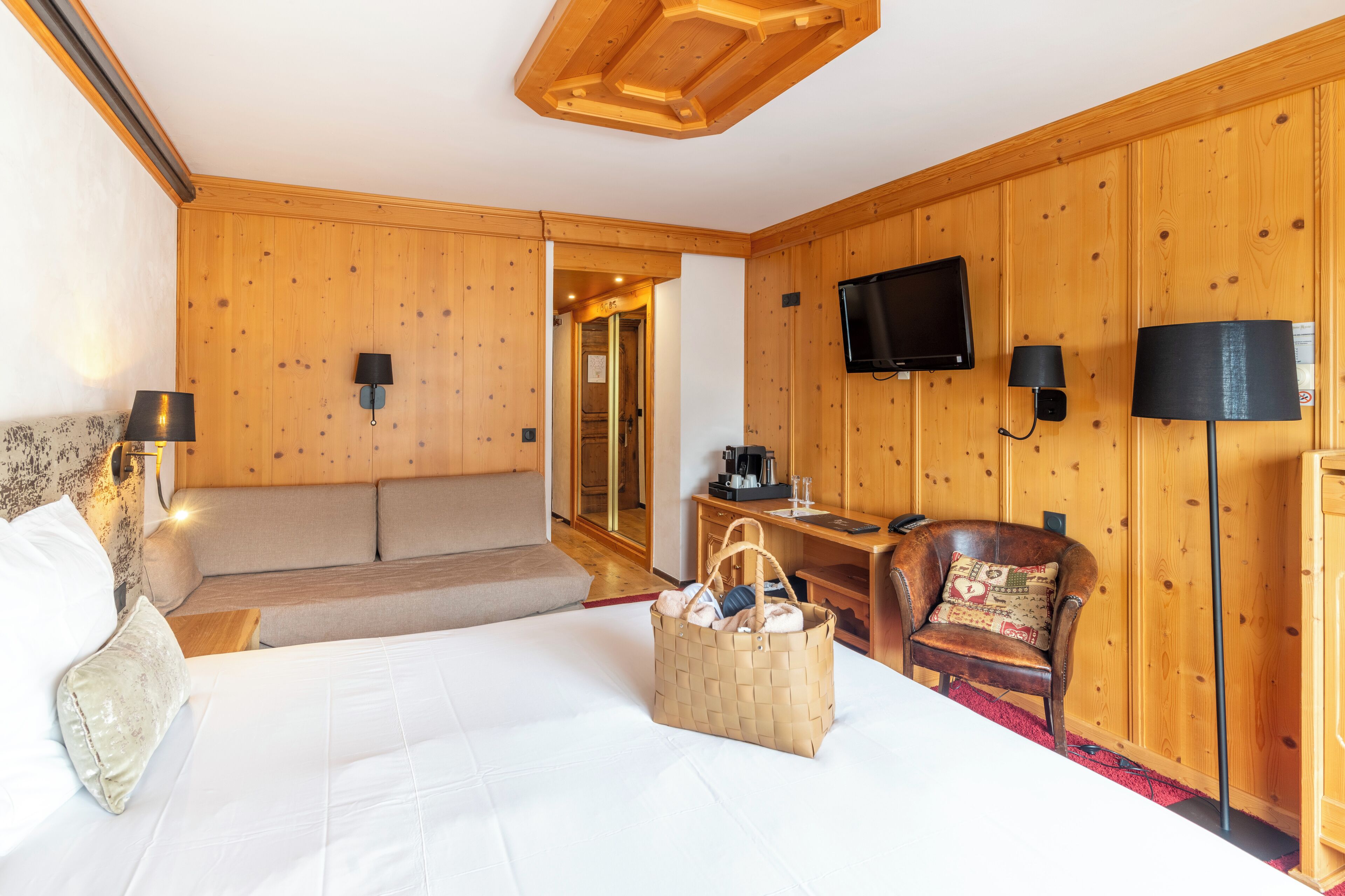 Ein Hotelzimmer mit einem großen Bett, einem Holzkopfteil, einem Schrank aus Holz, einem an der Wand befestigten Fernseher und einem Sessel mit Kissen.