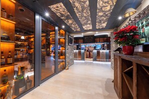 A bar area with a wooden counter, shelves with bottles, and a large potted plant. - Hôtel Macchi Restaurant & Spa (Chatel)