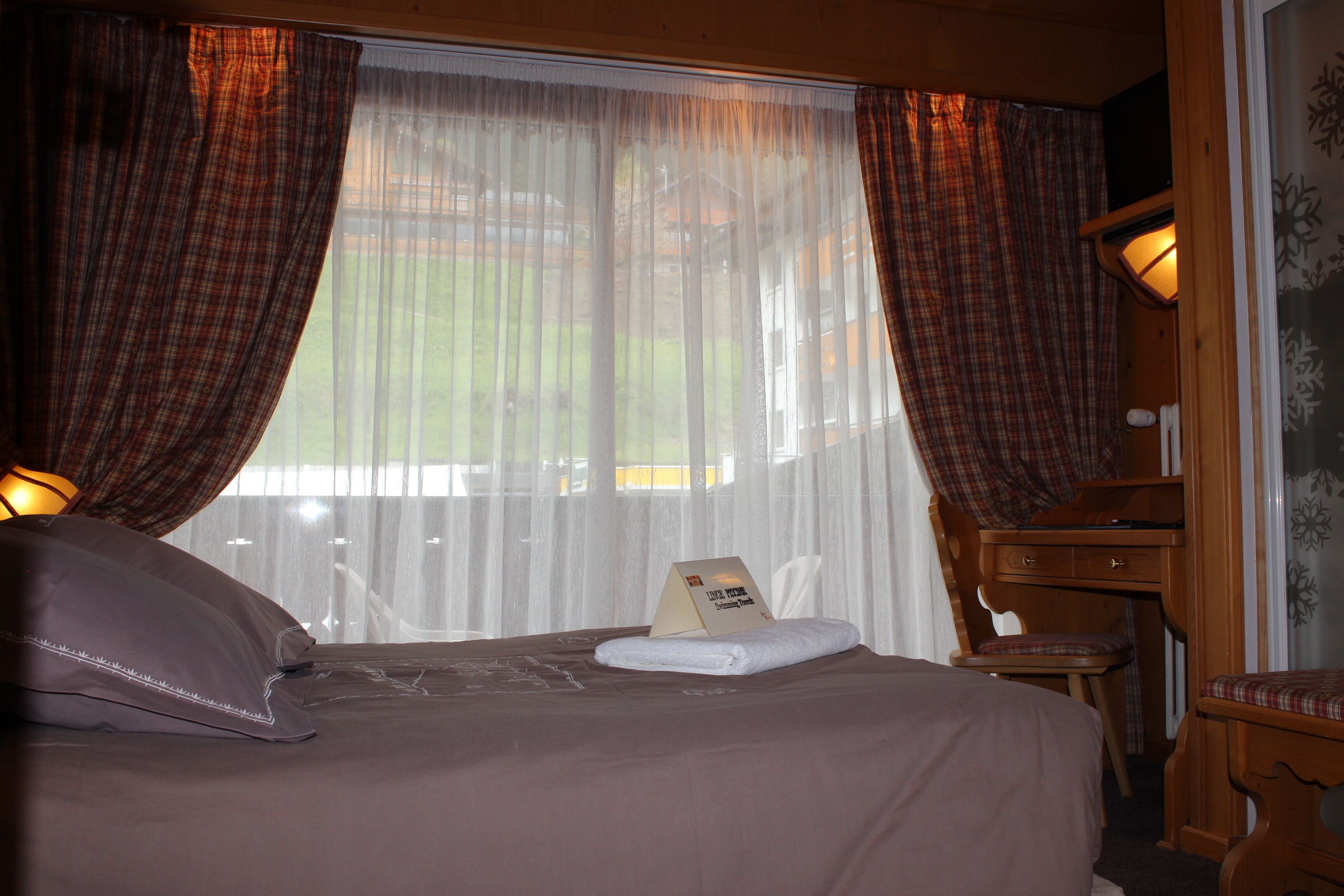 A hotel room with a bed, a chair, a desk, and a window with curtains.