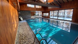 An indoor swimming pool with a clear view of the outdoors through large windows, wooden walls, and a stone-tiled floor. - Hôtel Macchi Restaurant & Spa (Chatel)