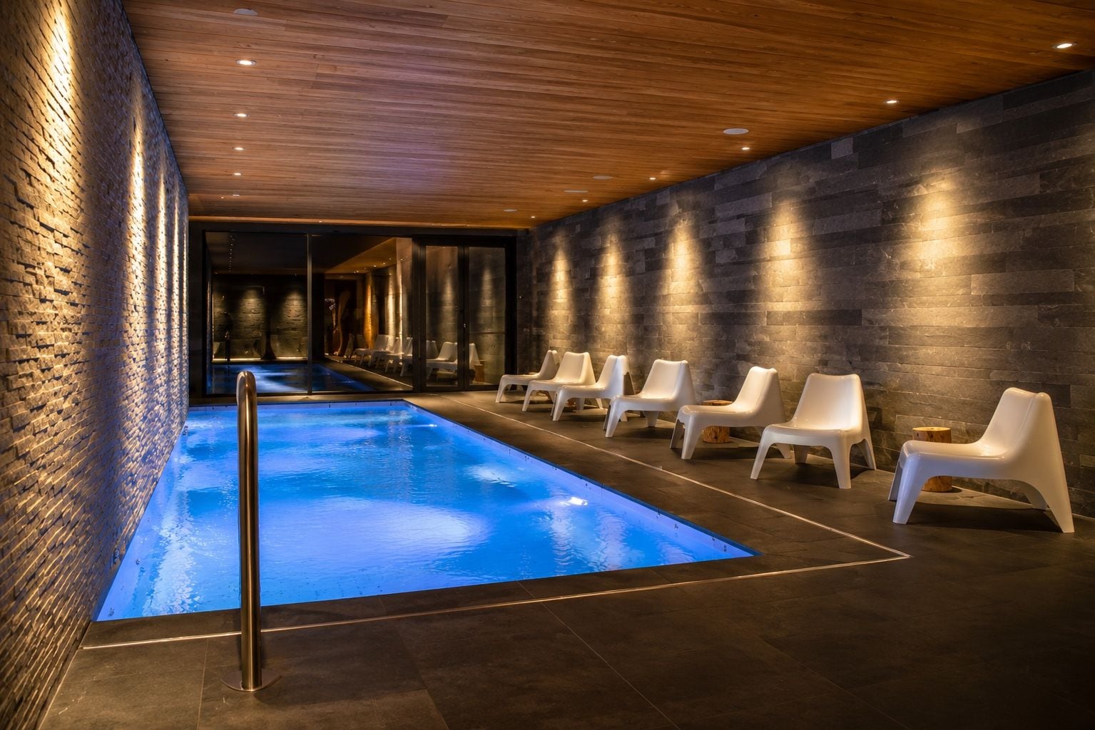A swimming pool with a wooden ceiling and stone walls, surrounded by white lounge chairs.