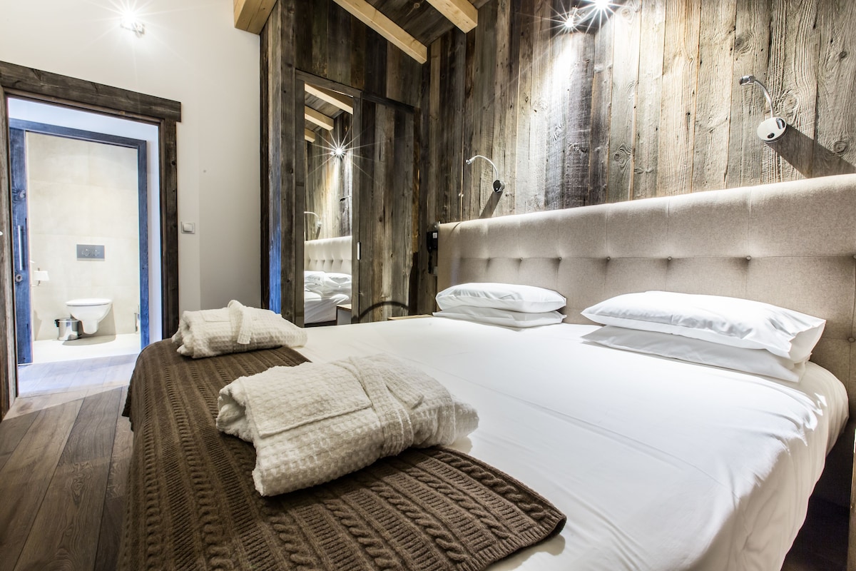 Une chambre à coucher avec un grand lit, des murs en bois et une salle de bain visible à travers une porte ouverte.