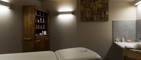 Un cuarto de spa con dos camillas, un mueble de madera, una lámpara fijada a la pared y un tocador de baño.