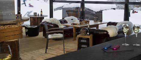 A cozy indoor setting with a bar area, leather seating, and a large window offering a snowy view.