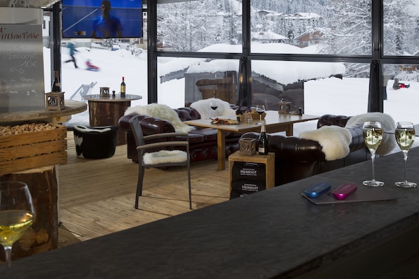 Un espace intérieur accueillant avec un bar, des fauteuils en cuir et une grande fenêtre donnant sur un paysage enneigé.