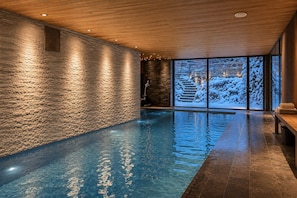Una piscina interior con paredes de piedra y vistas a un paisaje nevado a través de amplios ventanales.