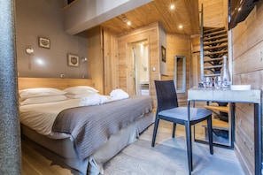 Een slaapkamer in een houten hutje, met een bed, stoel en een klein tafeltje met glazen.