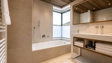 Une salle de bain moderne dotée d’une grande baignoire, d’une douche, d’un meuble-lavabo avec miroir et d’une fenêtre offrant une vue agréable.