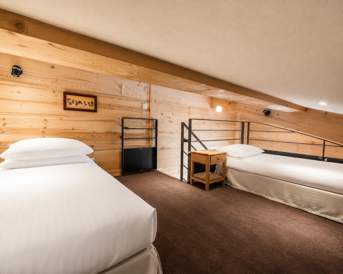 A room with two beds, a wooden wall, a small table, and a light fixture.