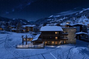 A hotel with multiple floors, a stone facade, and a snow-covered landscape in the background. - Le Crychar Hôtel & Spa - The Authentic Hotels Collection (Les Gets)
