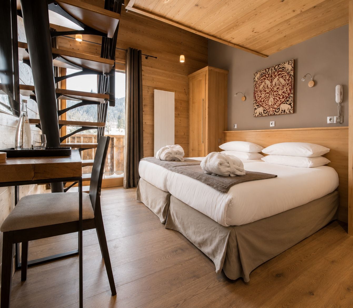 A wooden interior with a bed, a desk, and a view of the outdoors.