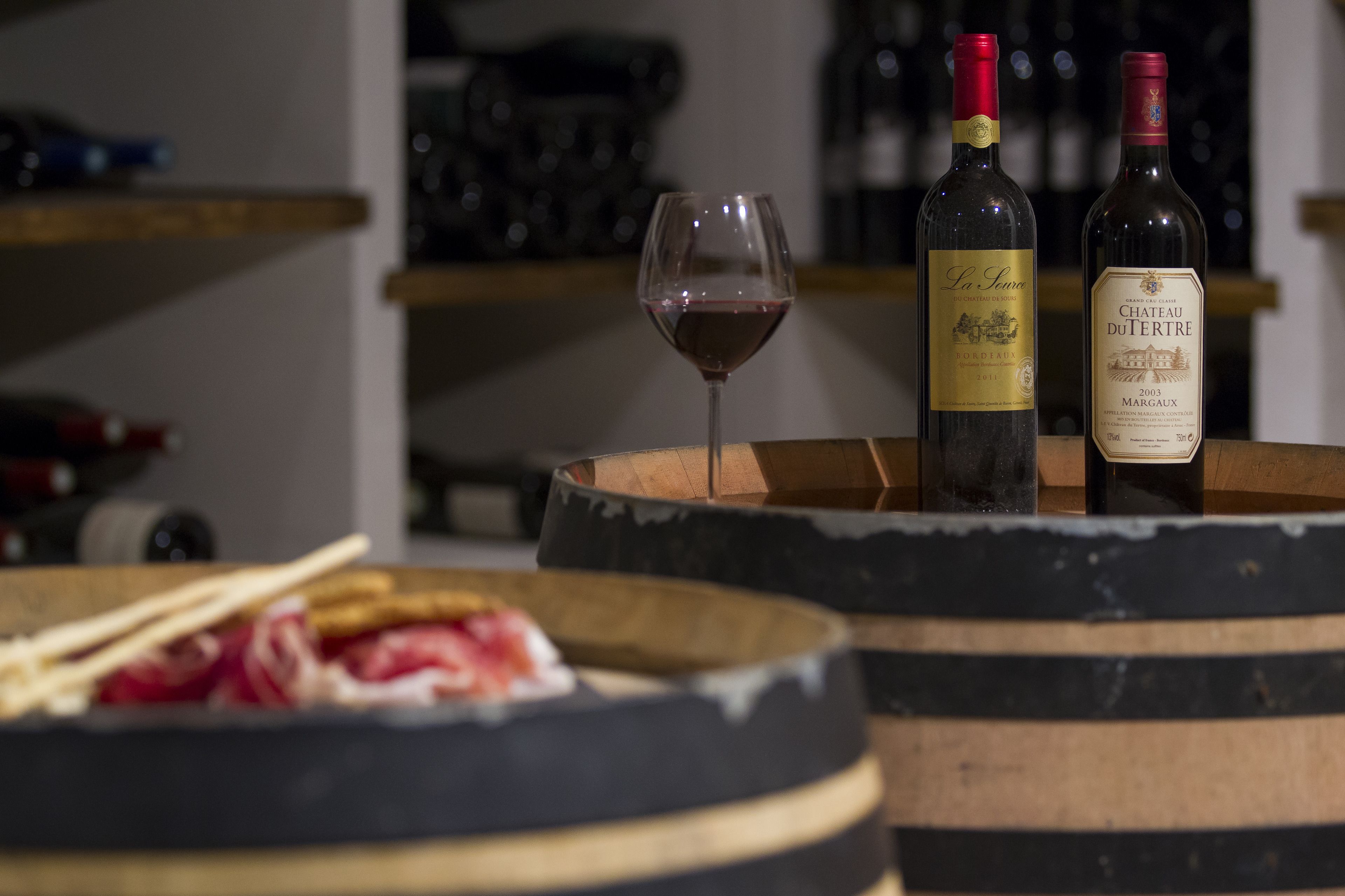 Deux bouteilles de vin et un verre de vin rouge posés sur une barrique en bois.