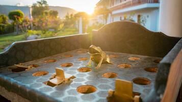 Un espacio al aire libre iluminado por el sol, con superficie de patrón hexagonal y círculos, que da vistas a un jardín ajardinado y un edificio con balcones.