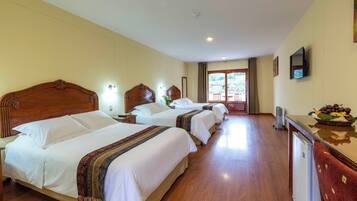 A hotel room with three beds, wooden headboards, bedside lamps, a flat-screen TV, a small refrigerator, and a window with a view of the outdoors.