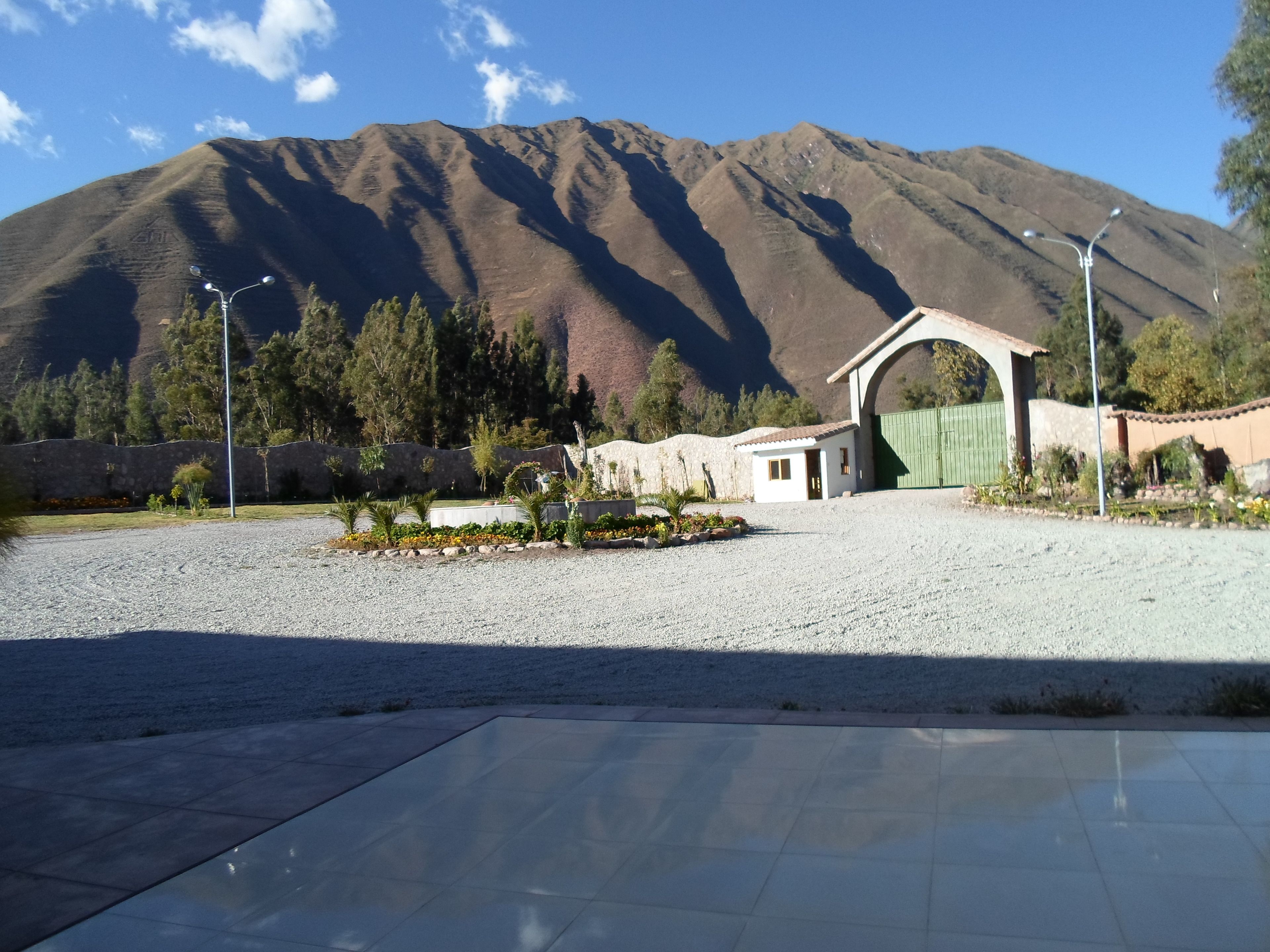 A paved area with a small building, a green gate, and a mountain in the background.