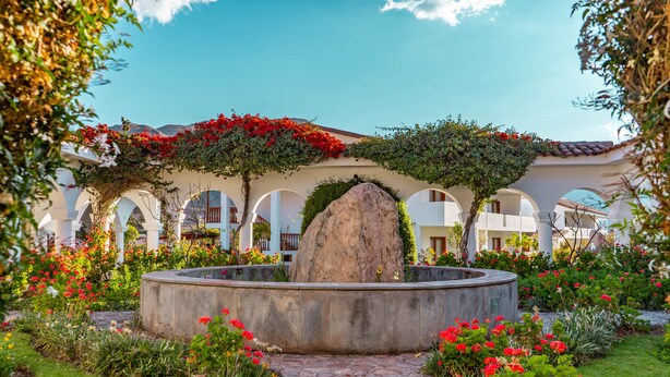 A courtyard with a central fountain, surrounded by arches and lush greenery. - Hotel Agustos Urubamba (Urubamba)