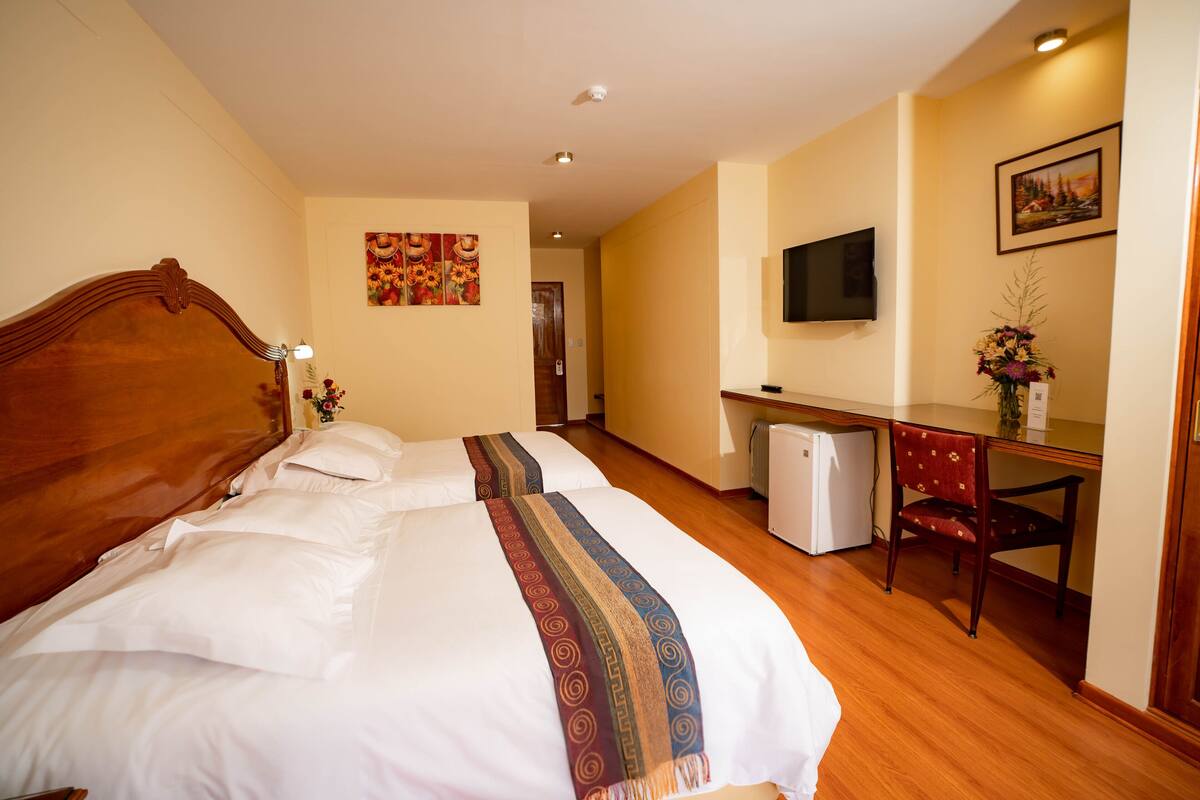 A hotel room with a large bed, a desk, a chair, a television, and a small refrigerator.