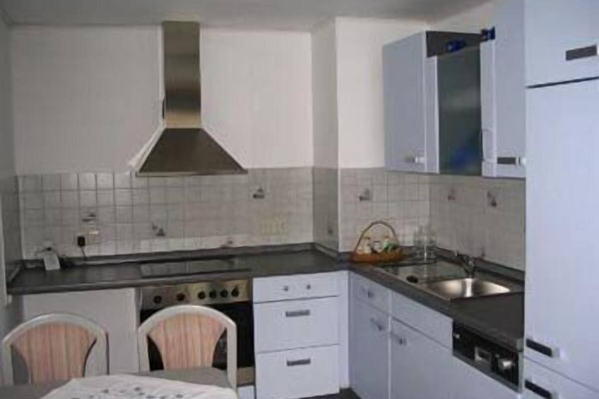A compact kitchen with white cabinets, a stainless steel range hood, a sink, and a stove.