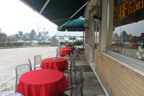 An outdoor seating area with round tables and chairs, covered by a green awning, and a storefront with a sign that reads "BF FLORI".