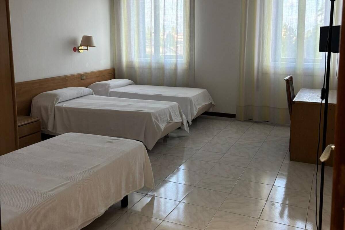 A hotel room with three beds, a desk, a chair, and a lamp.