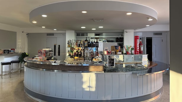 A modern bar area with a curved counter, stocked with various bottles and glasses, and a visible price tag. - Hotel Florida (Piove di Sacco)