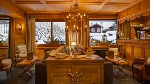 A cozy wooden interior with a chandelier, seating, and a view of a snowy landscape. - Chalet Hôtel Hermitage - Hotel Chalet de Tradition (Chamonix-Mont-Blanc)