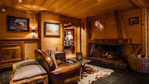 A cozy log cabin interior with a leather chair, a fireplace, and framed artwork on the walls. - Chalet Hôtel Hermitage - Hotel Chalet de Tradition (Chamonix-Mont-Blanc)