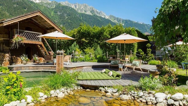 A wooden cabin with a deck, outdoor seating, and a small pond. - Chalet Hôtel Hermitage - Hotel Chalet de Tradition (Chamonix-Mont-Blanc)