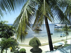 Blick auf einen Strand mit Palmen, einem kleinen Boot und einer Laube am Wasser.