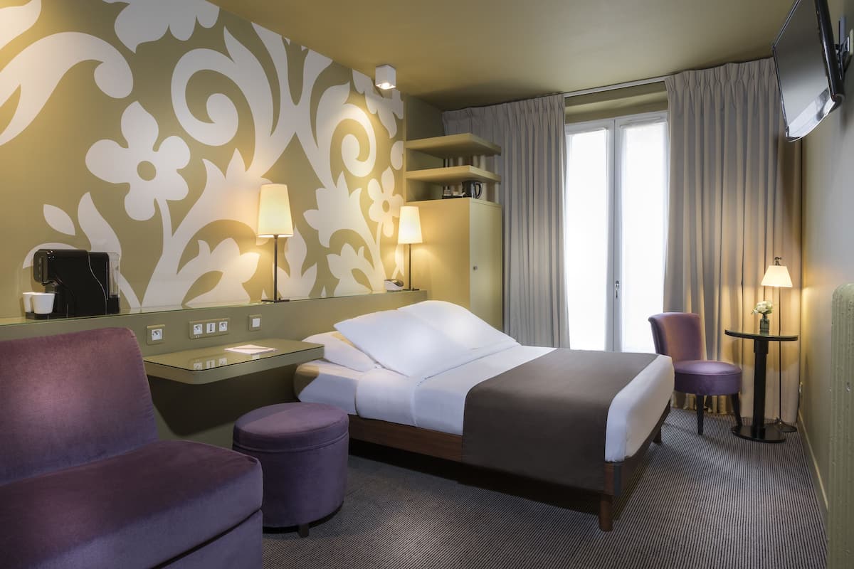 Quarto de hotel com cama, escrivaninha, cadeira, mesinha e espelho.