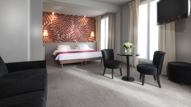 A hotel room with a bed, two chairs, a small table with a vase, a TV, and a zebra-patterned wall. - Gardette Park Hotel (Paris)