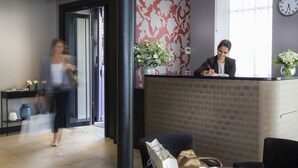 A reception area with a receptionist desk, a clock on the wall, and a vase with flowers. - Gardette Park Hotel (Paris)