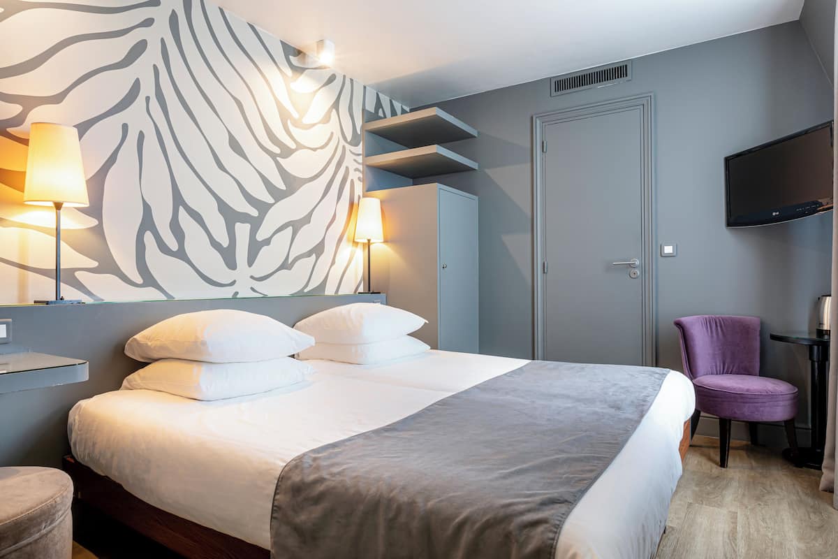 Quarto de hotel moderno com uma cama grande, parede com padrão de zebra, televisão de tela plana e uma cadeira roxa.