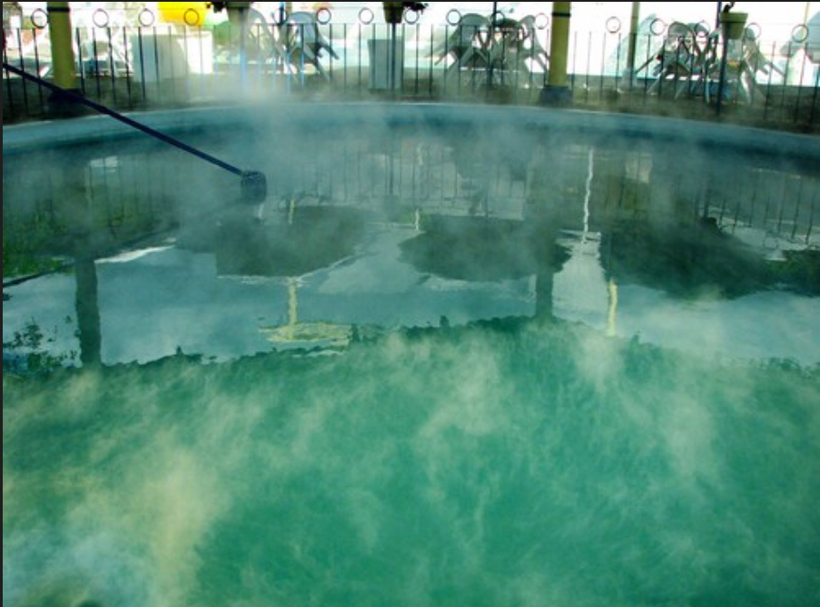 Amplio espacio interior con techo alto y una zona central que parece ser una piscina o fuente de agua, rodeada de barandas metálicas.