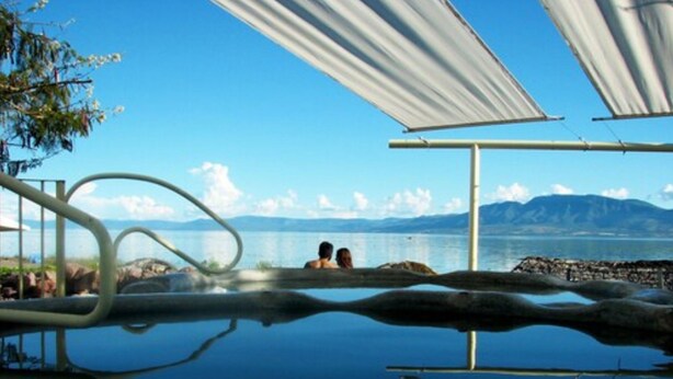 A serene outdoor swimming area with clear blue water, a view of the sea, and mountains in the distance. - Hotel Balneario San Juan Cosalá (Jocotepec)
