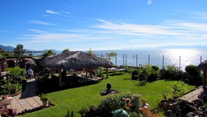 A garden with a thatched-roof structure, a lawn, and a view of the sea. - Hotel Balneario San Juan Cosalá (Jocotepec)