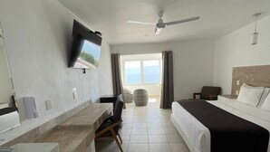 A hotel room with a bed, a desk, a chair, a television, a ceiling fan, and a window with curtains. - Hotel Balneario San Juan Cosalá (Jocotepec)