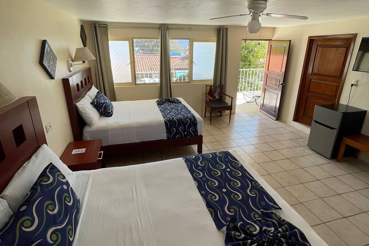 Ein Hotelzimmer mit zwei Betten, einem Deckenventilator, einem Balkon und einer Küchenzeile.