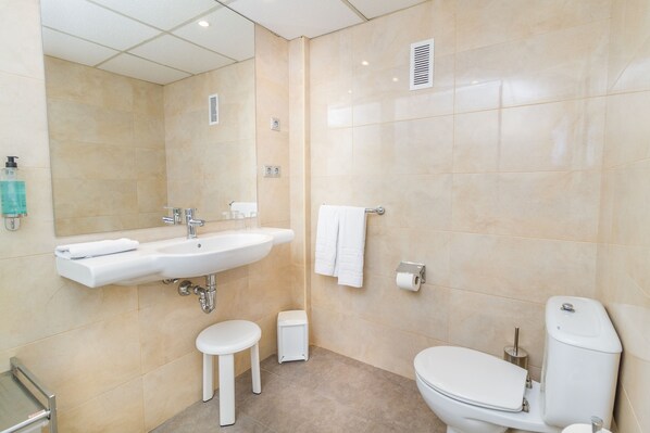 Un baño moderno con lavamanos, inodoro y un taburete pequeño.