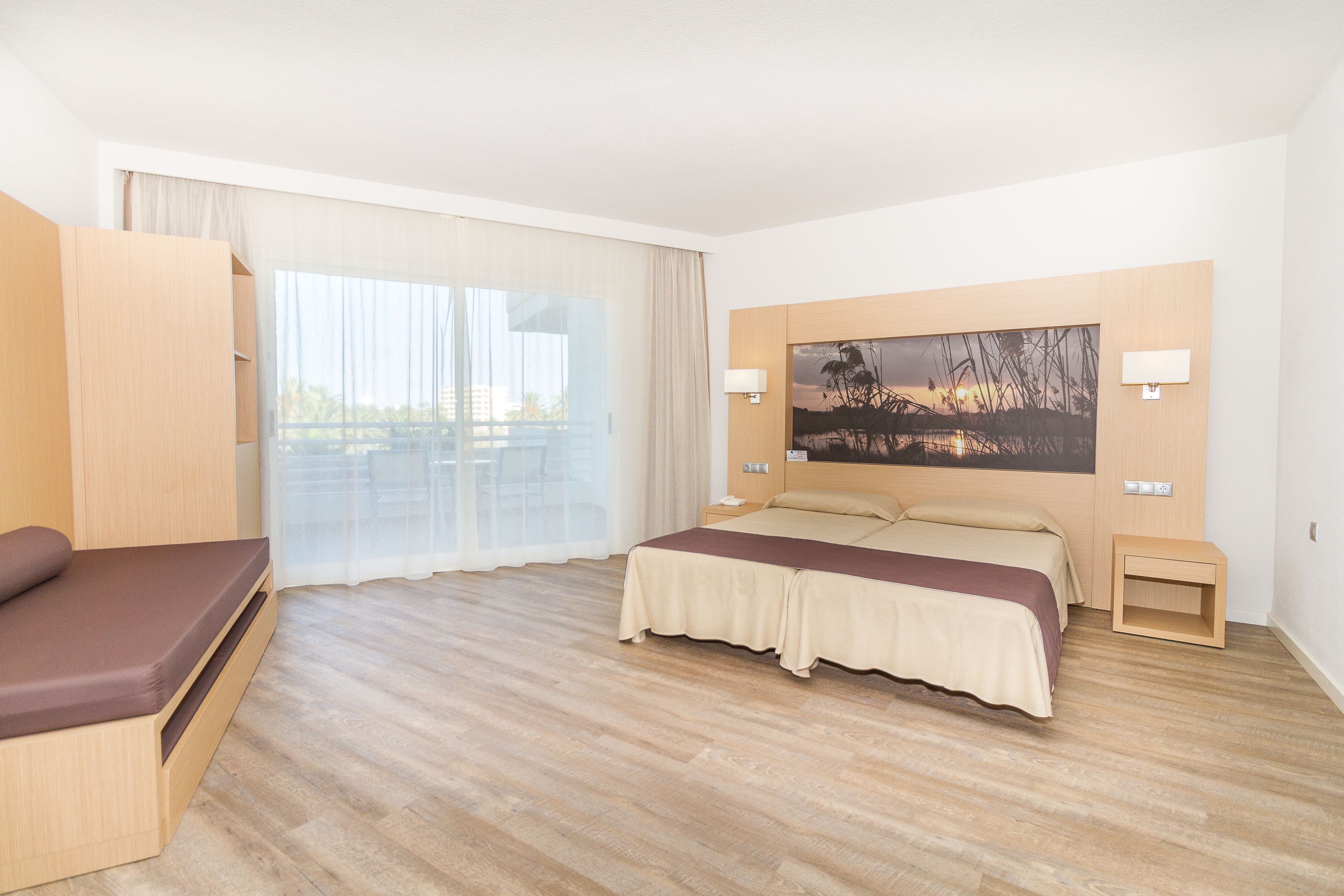 Hotelkamer met een bed, een sofa, een groot raam met gordijnen, een schilderij aan de muur en een houten vloer.